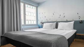 Modern standard double room with a double bed, grey bedspread, grey curtains and wall art at the Quality Hotel Grand Kristianstad 